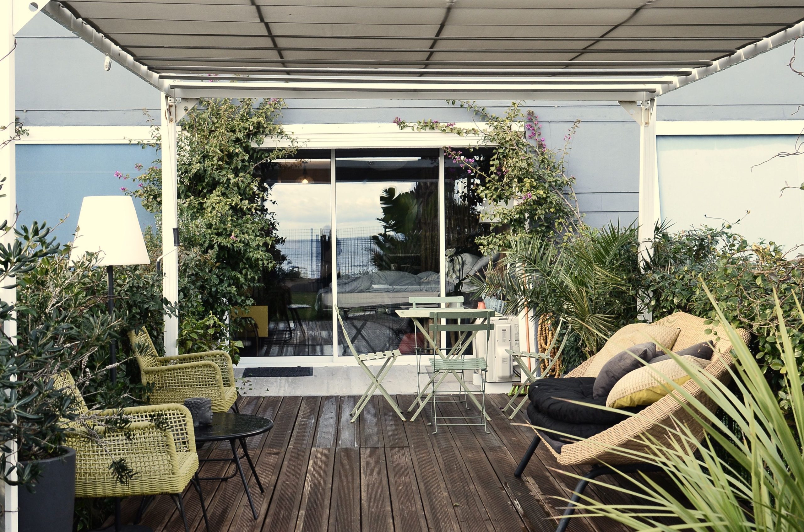 Véranda en bois avec fauteuils rotin et plantes exotiques